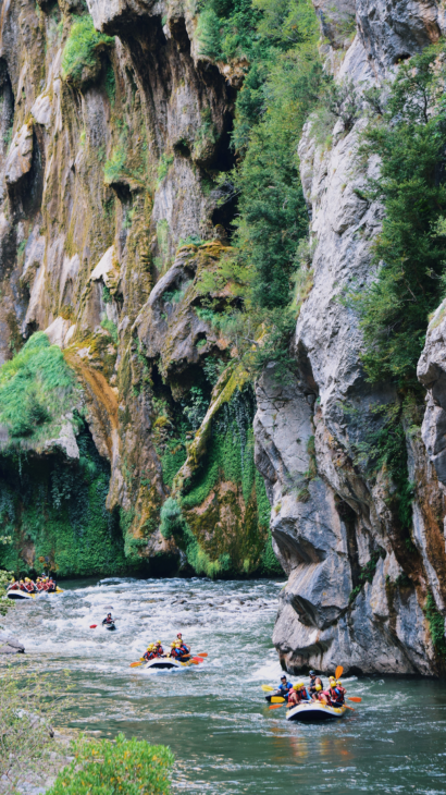 3 rafts and a ducky floating down a river in a tall and mossy canyon.
