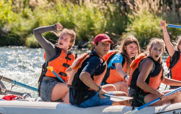 group of students on a araft laughing and celebrating passing through whitewater rapids