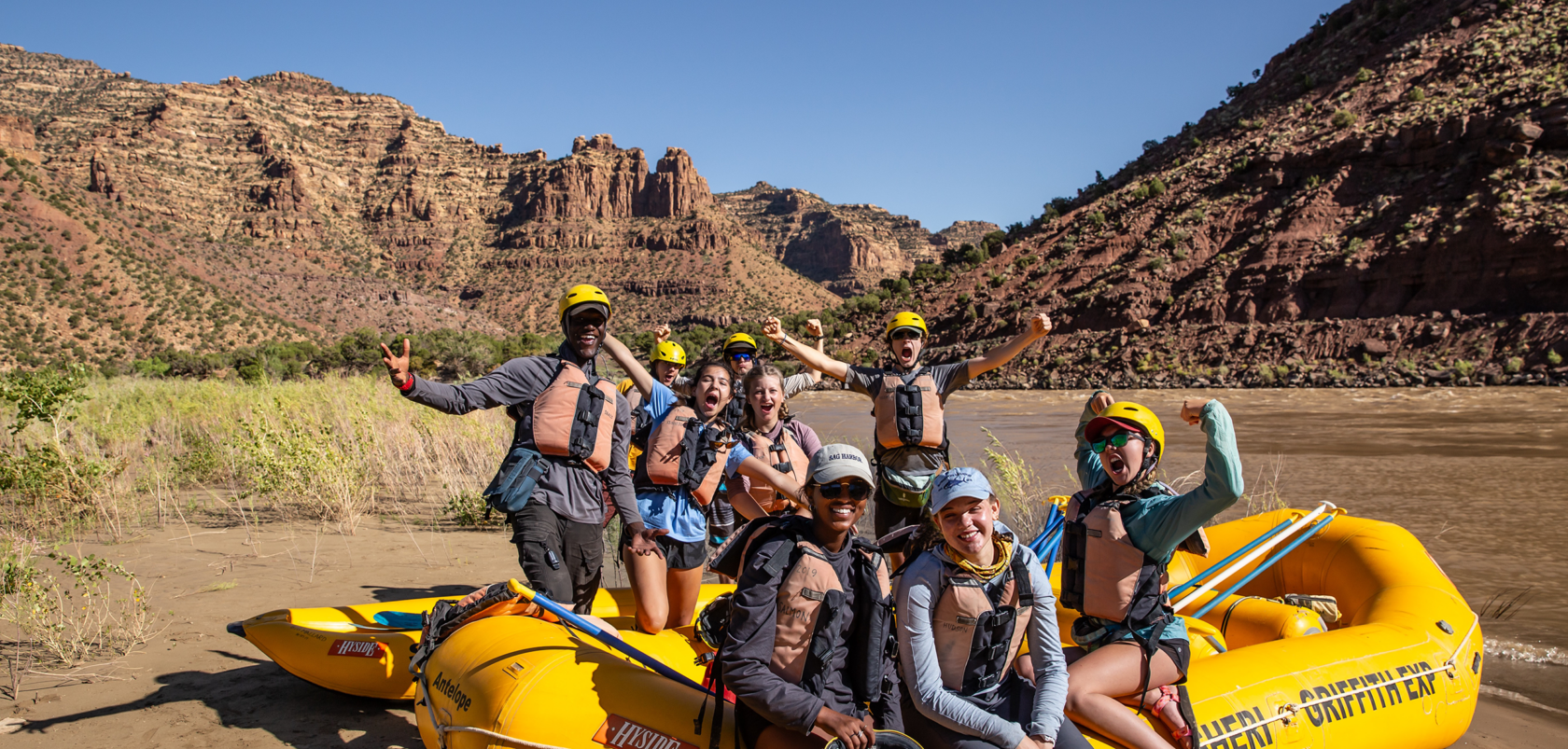 Group of people with their arms in the air on a whitewater raft in the desert.