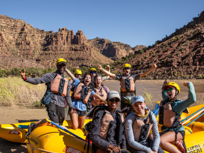 Group of people with their arms in the air on a whitewater raft in the desert.