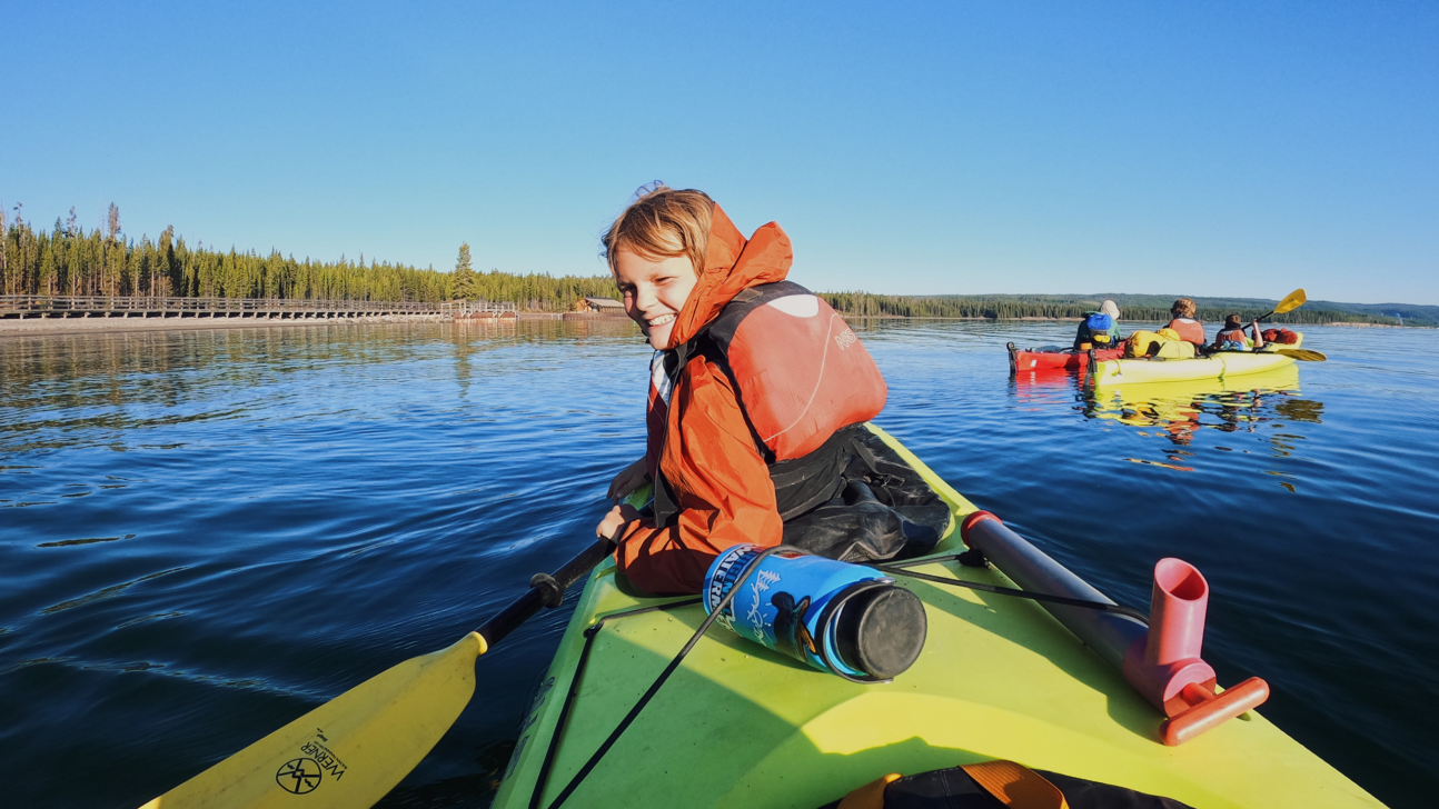 Young boy smiling in a sea kayak on a calm lake.