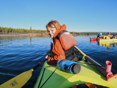 Young boy smiling in a sea kayak on a calm lake.