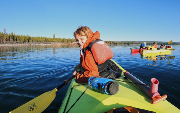 Young boy smiling in a sea kayak on a calm lake.