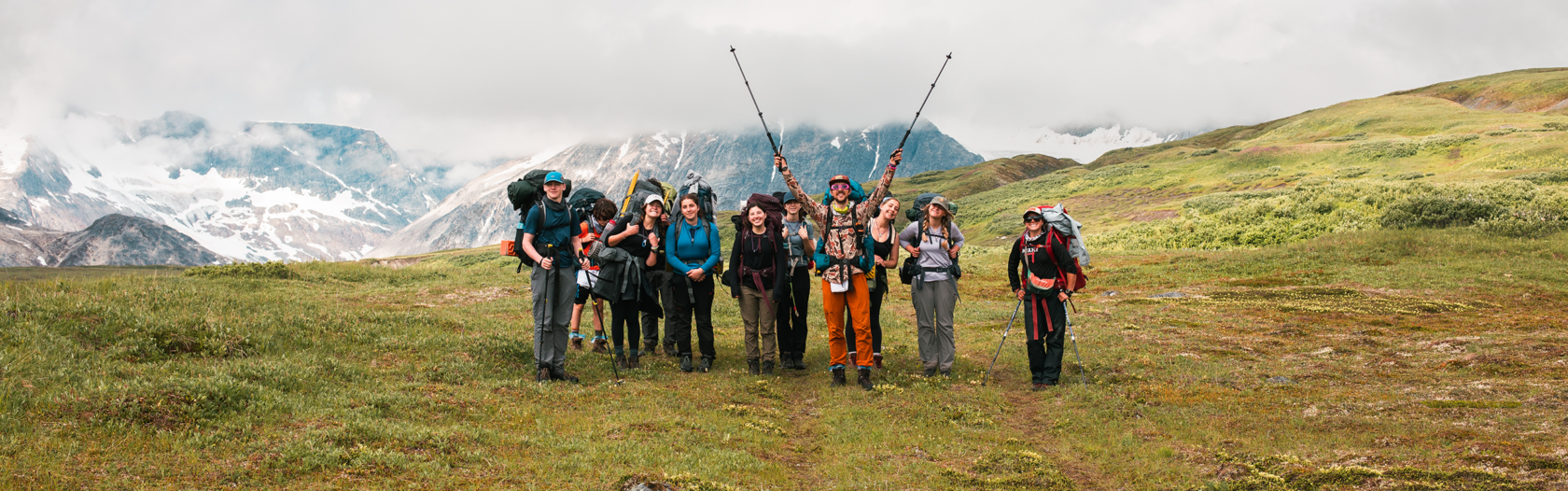Group of people hiking in a field in front of large Alaskan mountains.