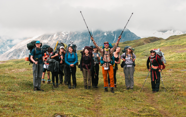 Group of people hiking in a field in front of large Alaskan mountains.