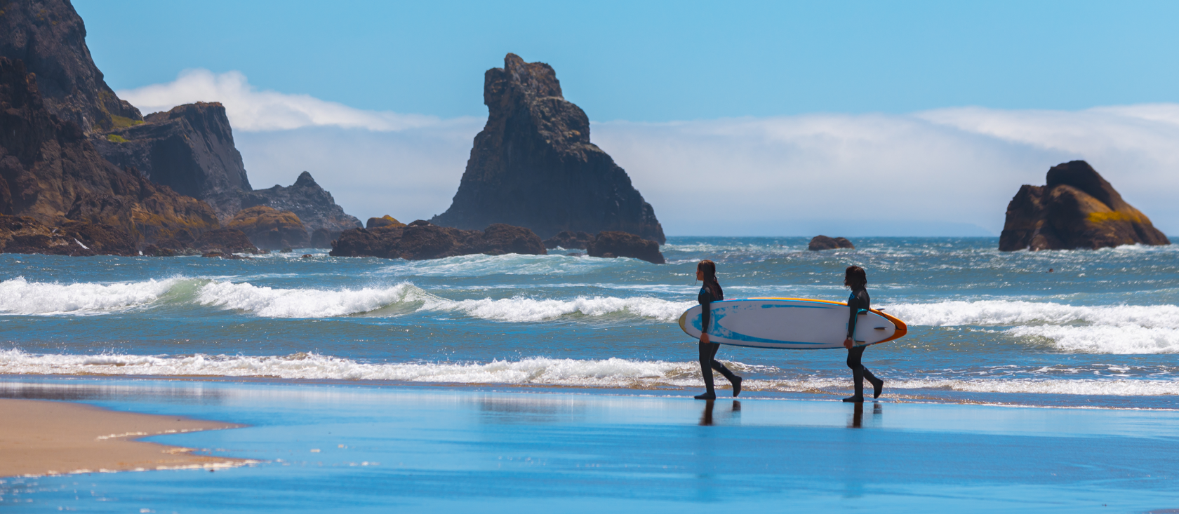 Two people carrying a surfboard on the pacific coast.