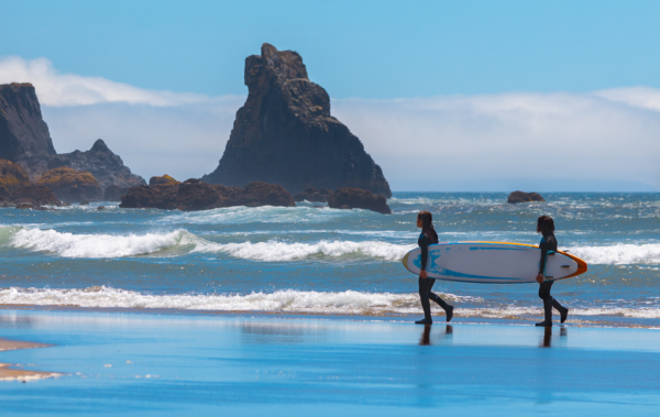 Two people carrying a surfboard on the pacific coast.