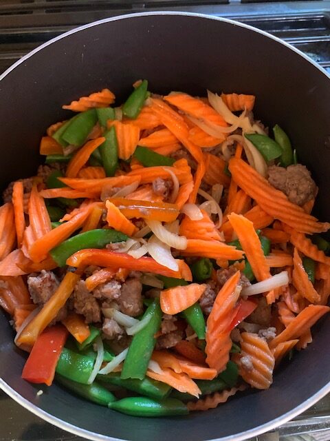Sautéed carrots, peppers, onion, and meat in a pot. 