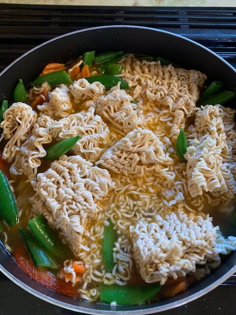 Pot of ramen noodles and vegetables in broth.