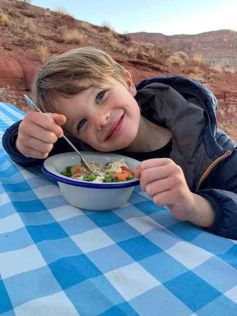 Young boy with a bowl of ramen noodles in the desert at a picnic table.