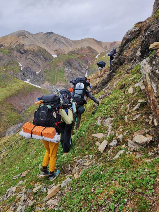 People backpacking along a ledge in the alaskan wilderness.