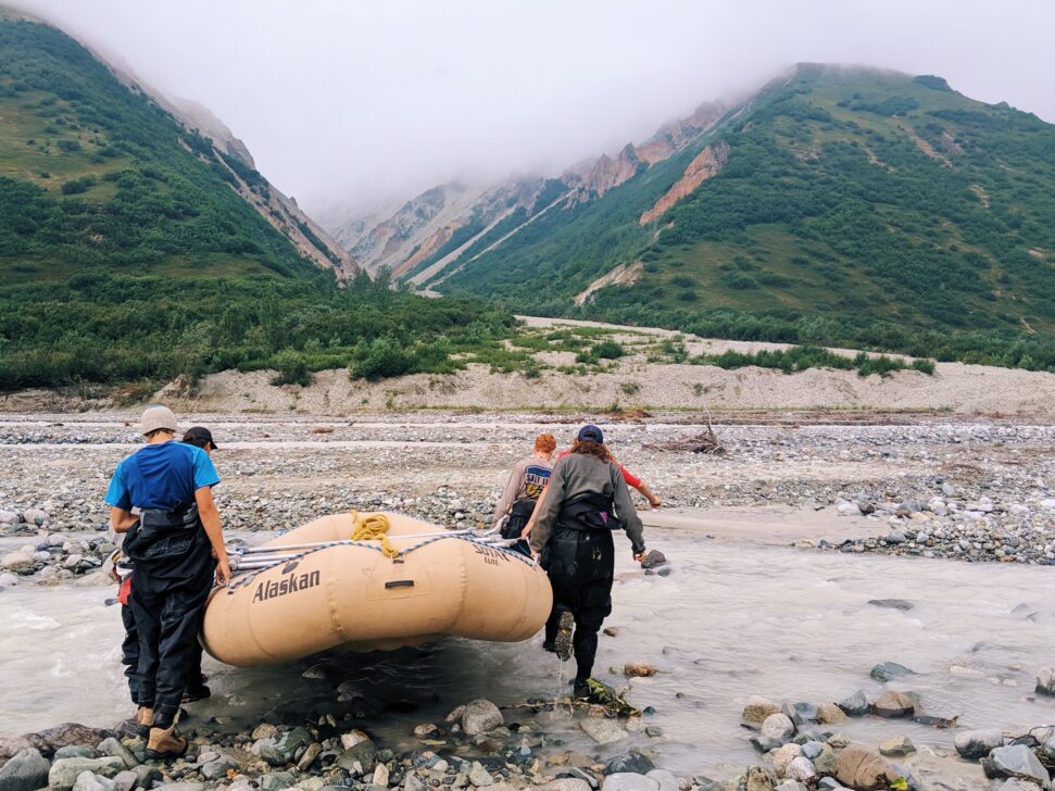 People carrying a whitewater raft into a river in the mountains.