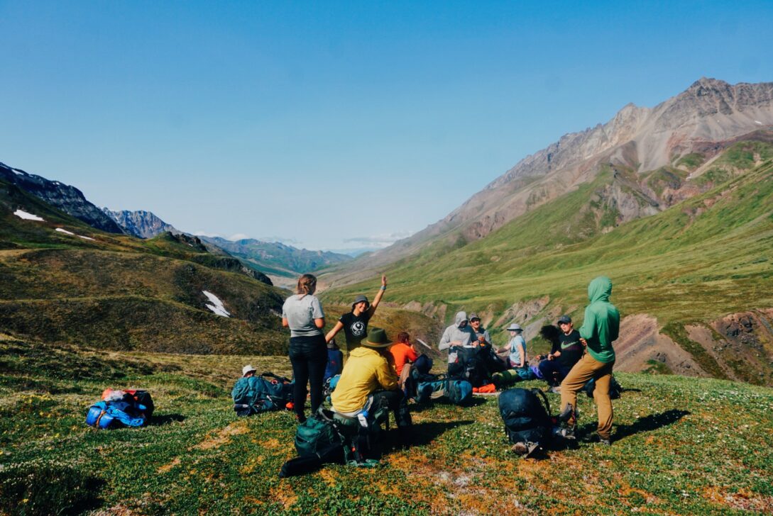 Group of people sitting in a circle in an alaskan mountain range.