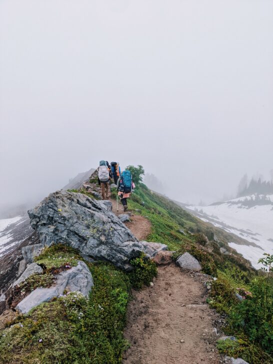 People hiking on a foggy ridge.