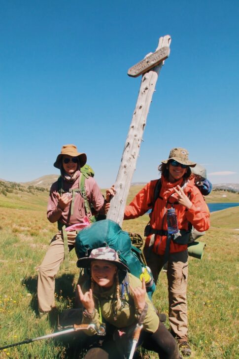 Three people posing in front of a trail marker sign.