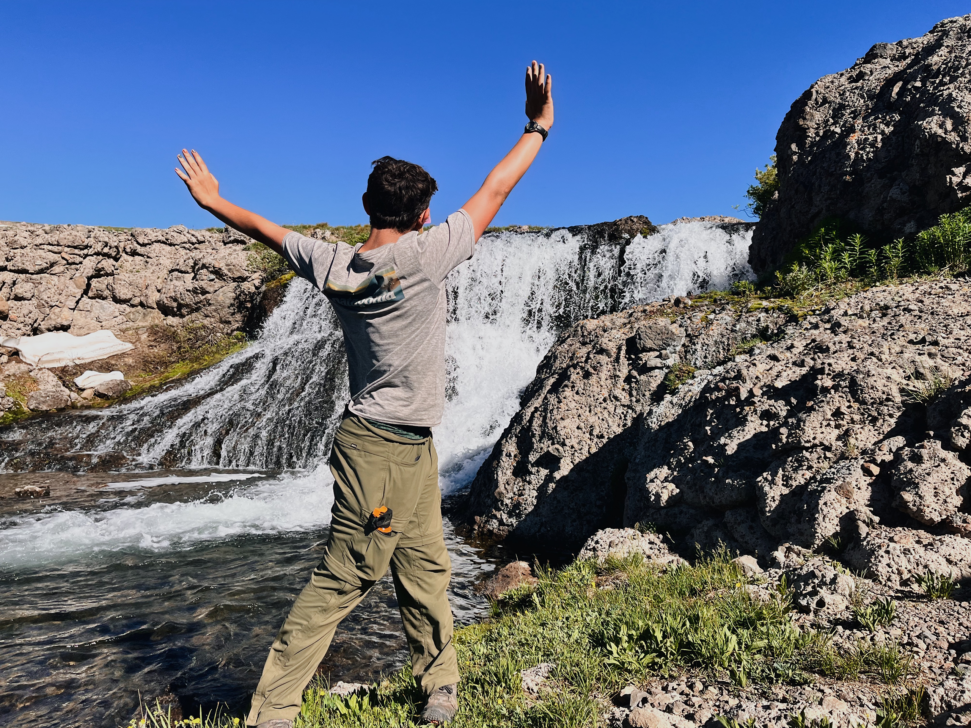Person with their arms in the air in front of a waterfall.