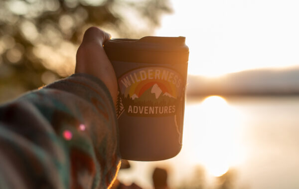 travel mug with a Wilderness Adventures sticker on it in front of the sunset