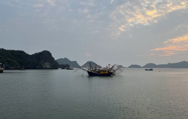 Cloudy sunset over the ocean and rocky coast of Vietnam. Oldschool fishing boat in the center of the image with many flags and nets.