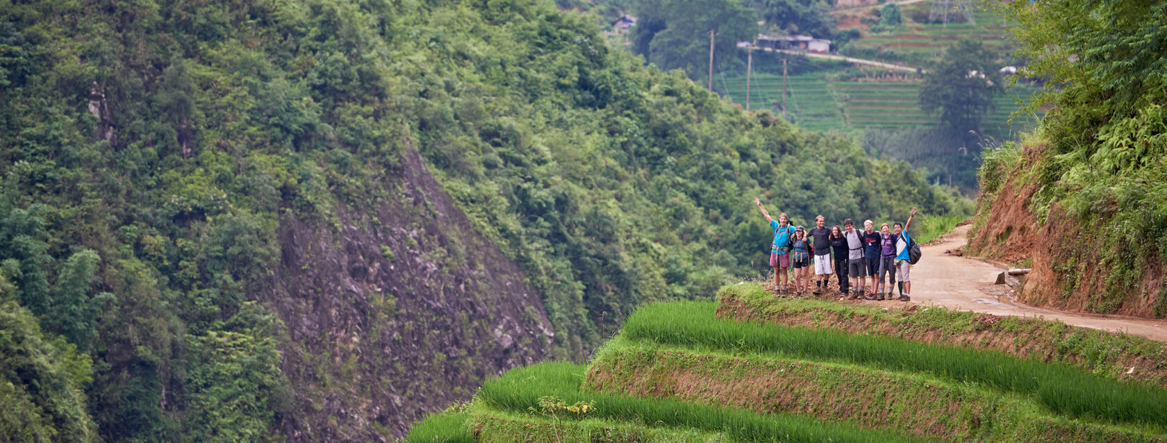 Group of travelers at the edge of a trail trekking through the fields of a village in Vietnam.