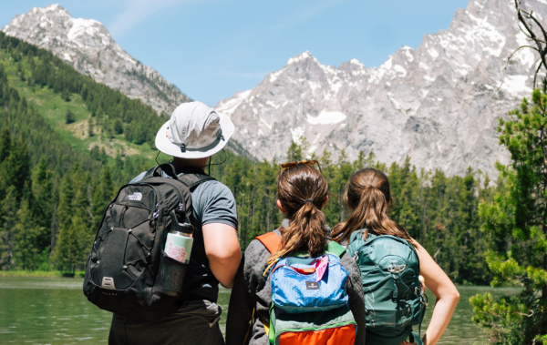 Three people looking out on a lake with the Tetons in the background.