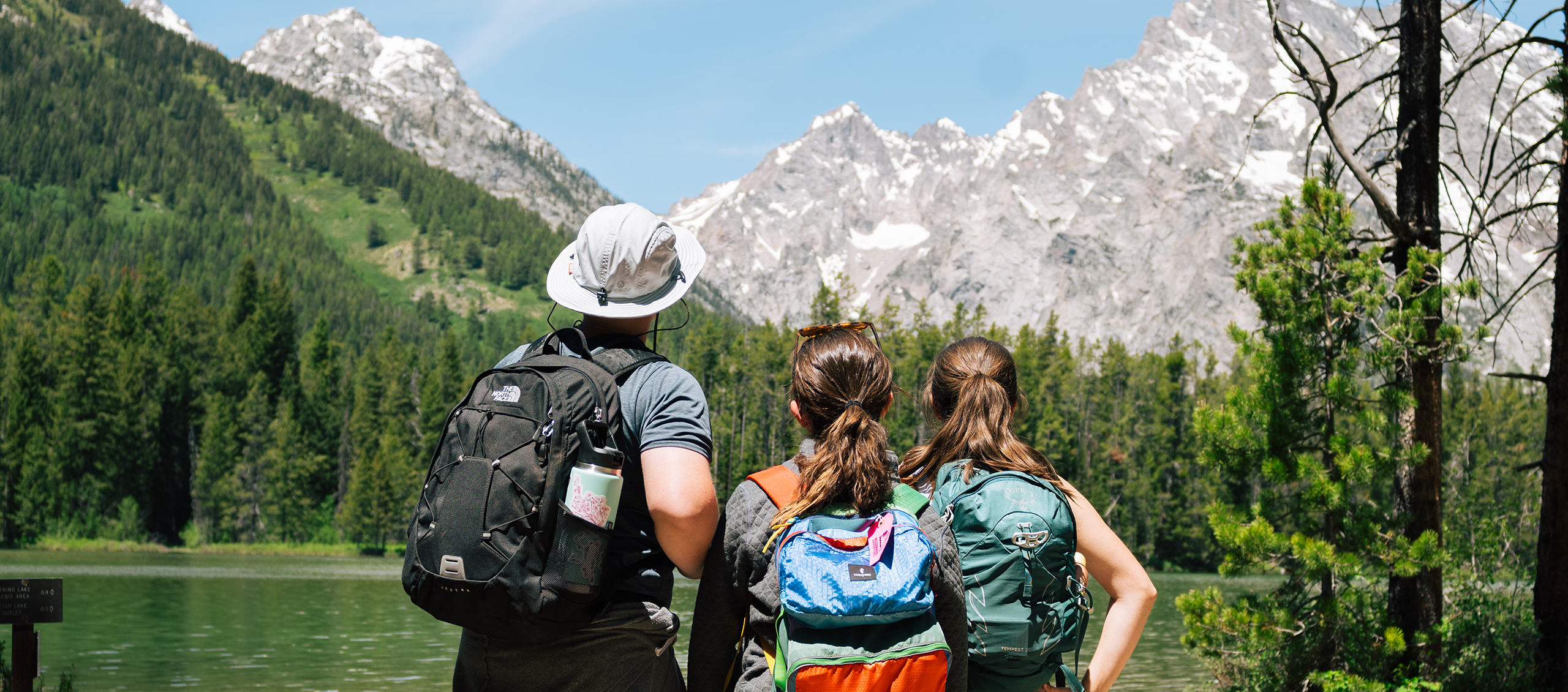 Three people looking out on a lake with the Tetons in the background.