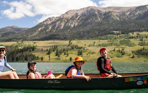 Four campers paddling in a canoe on a lake.