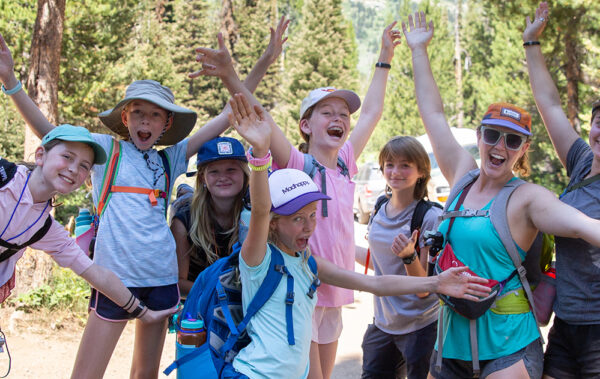 Group of girls with their hands in the air and big smiles on a hike.