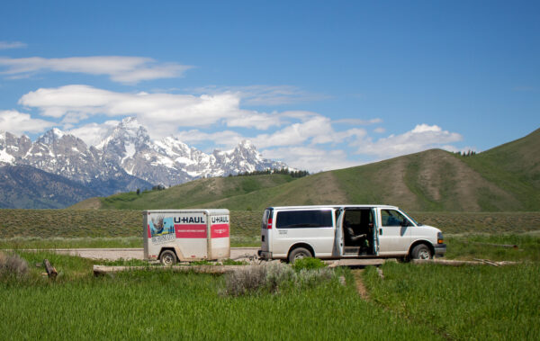 15 passenger Ford van with a uHaul trailer attached in front of the Tetons.