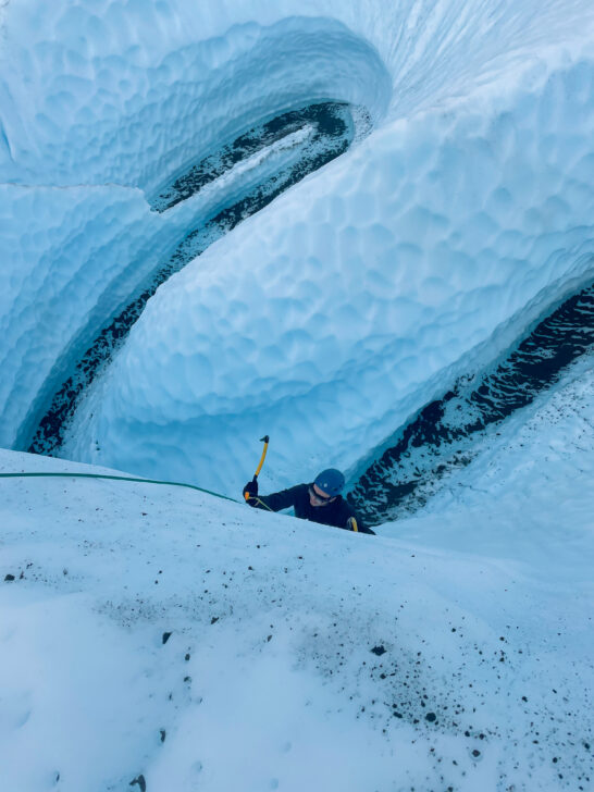 View from above of a person ice climbing up a large ice wall.