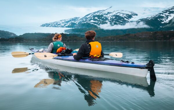 Two people looking to the horizon of mountains while kayaking on smooth water.