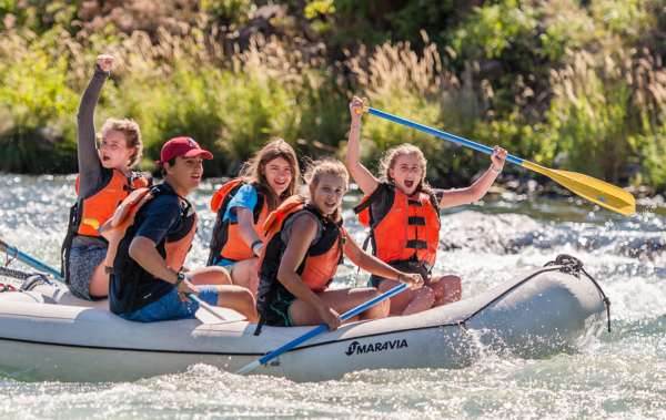 Group of campers on an inflatable raft floating down the river with excited looks on their faces.