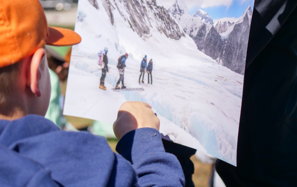 Young boy admiring a photo of people mountaineering.