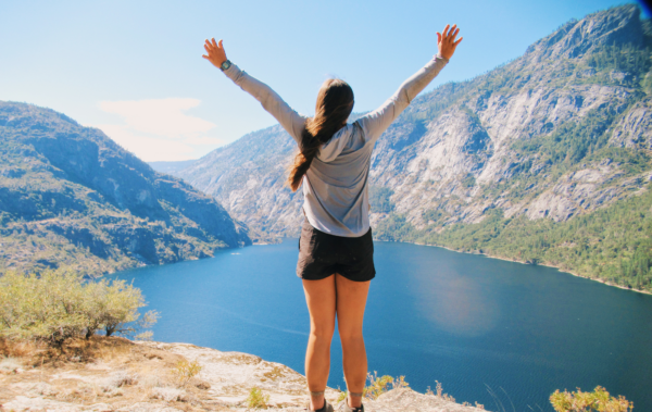 Girl with both arms in the air at a beautiful Yosemite overlook.