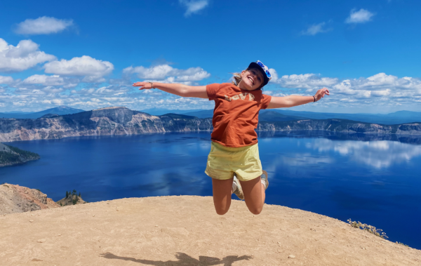 Girl jumping in the air in front of a big blue lake.