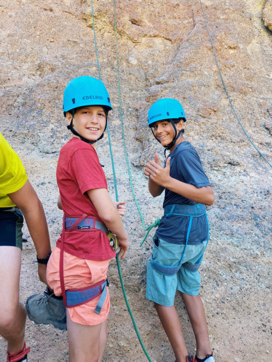 Two young boys smiling at the base of a rock climbing route.