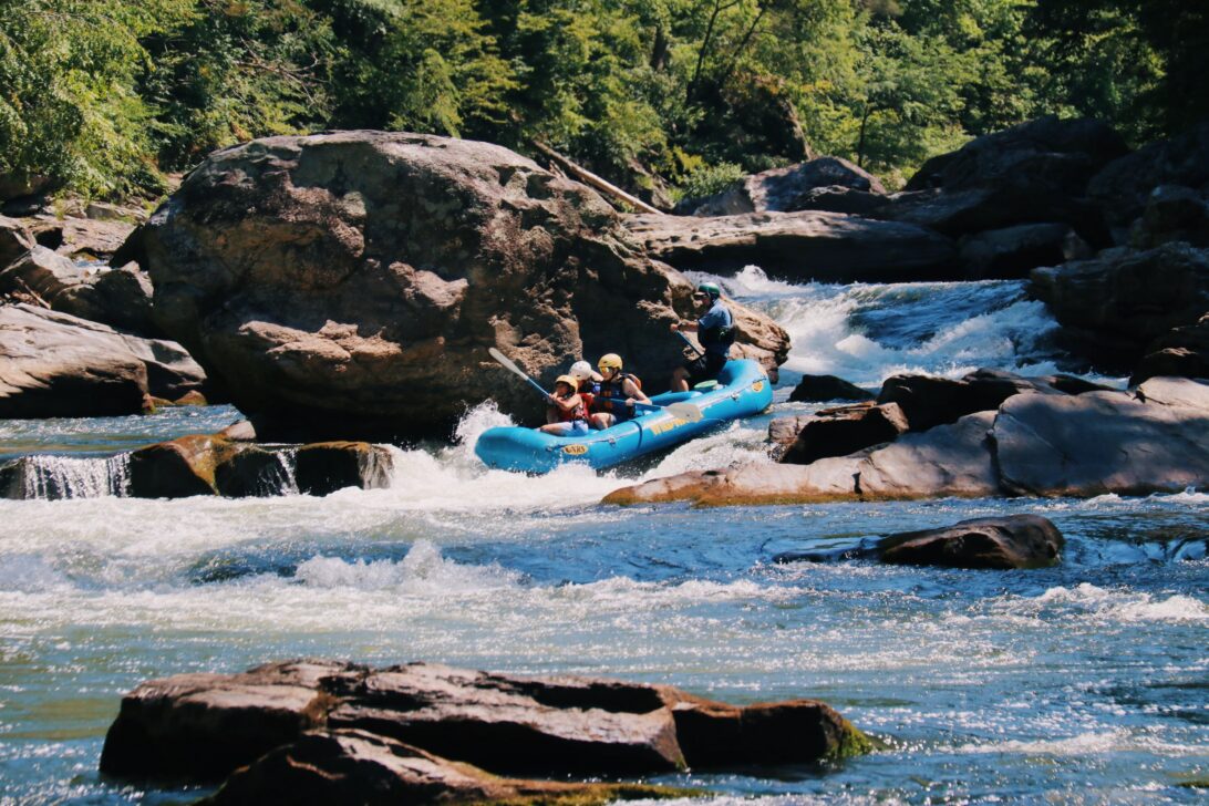 Blue raft going through rapids in a rocky river.