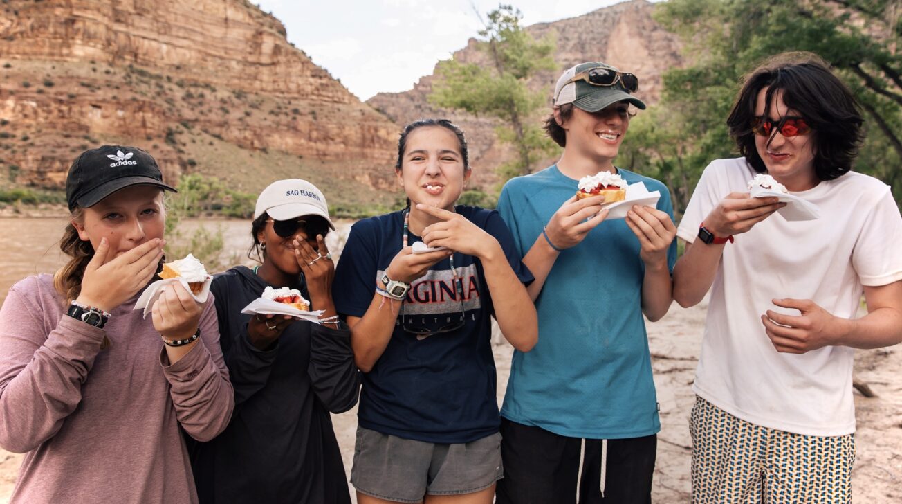 Five people eating strawberry shortcake in the desert laughing.