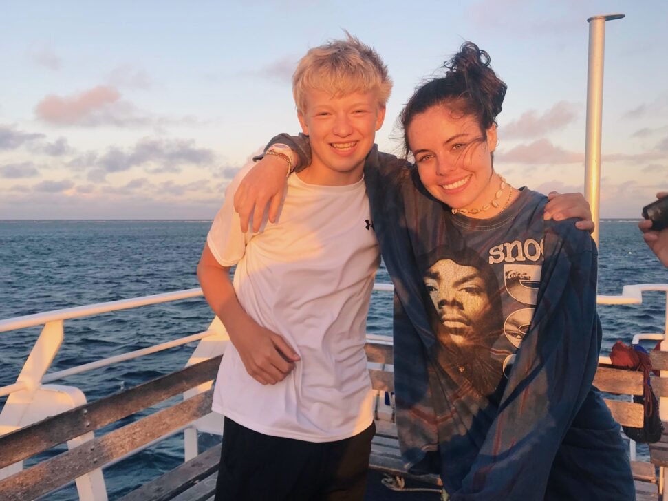 Two people with their arms around each other on a boat in the sunset.