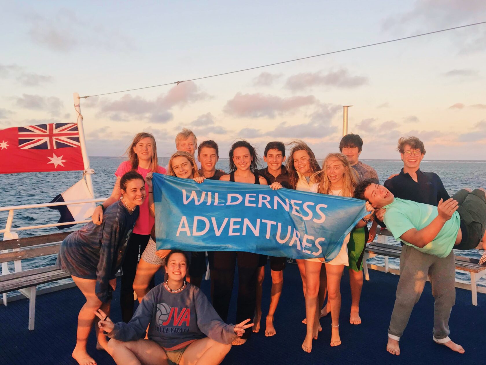Group of people holding up a Wilderness Adventures banner on a boat with the Australian flag in the background.