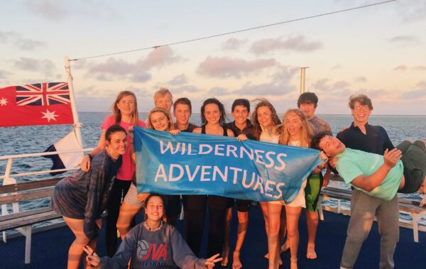 Group of people holding up a Wilderness Adventures banner on a boat with the Australian flag in the background.