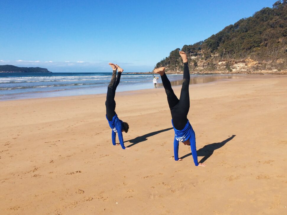 Two people doing handstands on the beach.