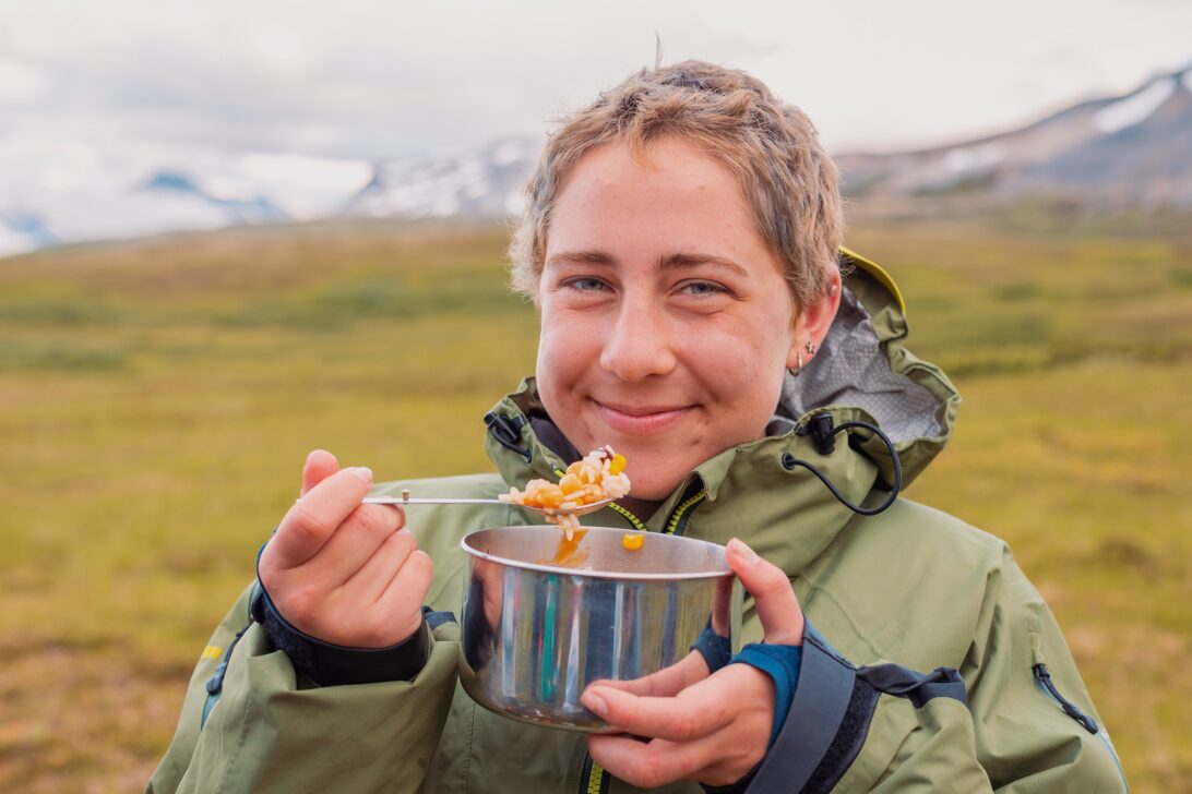 Person smiling and eating a rice bowl in the mountains.