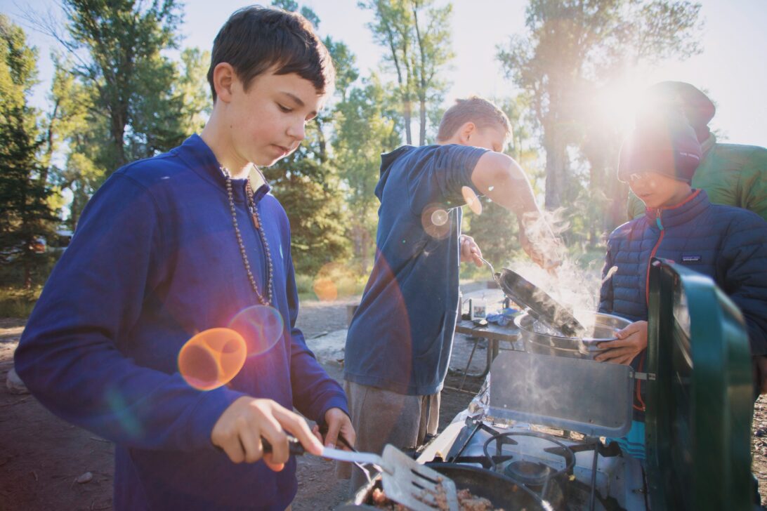 Kids cooking on a camp stove with the sun shining through behind them.