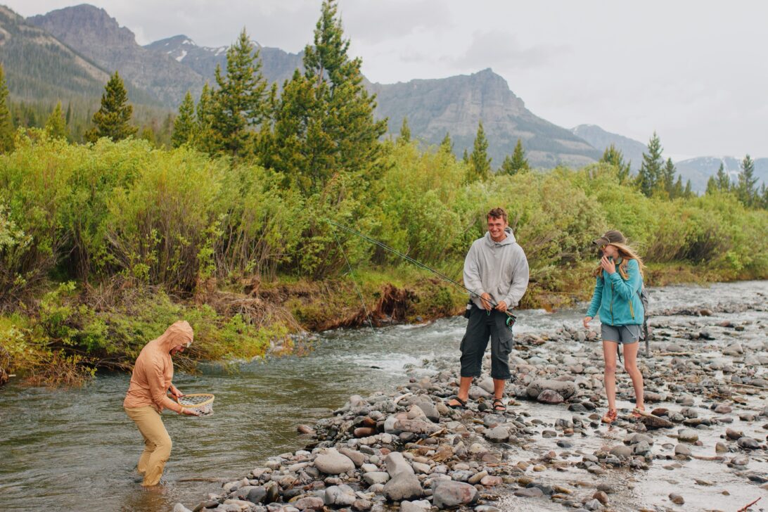 Three people catching a fish on a rocky river shore.