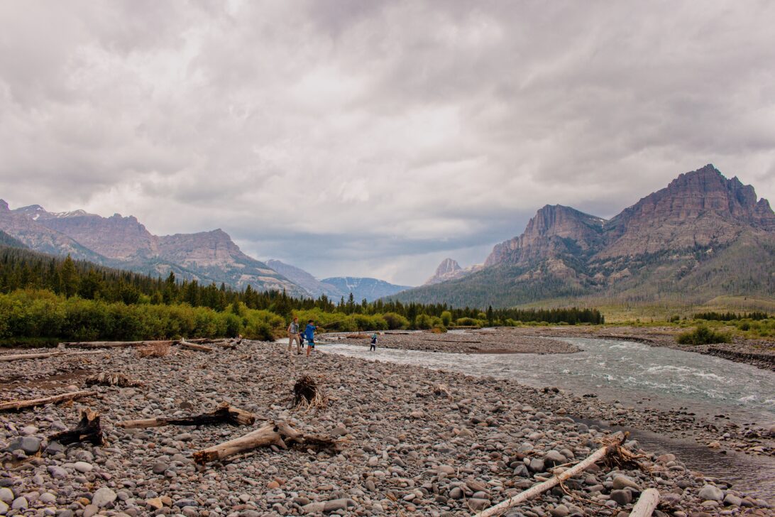 People walking in the distance with a river, mountains, and dark clouds.