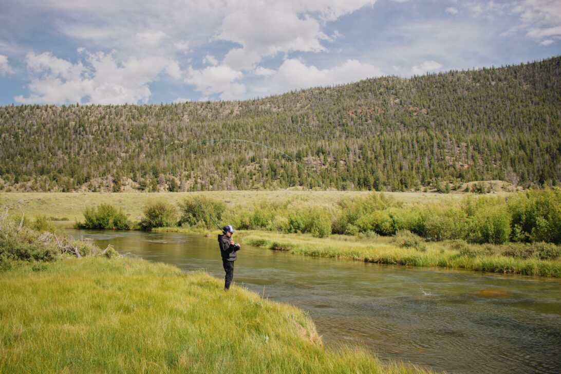 Person fishing in a vast green field and flowing river.