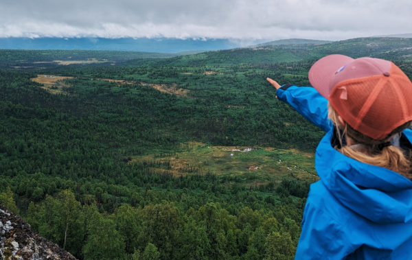 Person in a baseball hat point out to the horizon of a vast valley in Alaska.