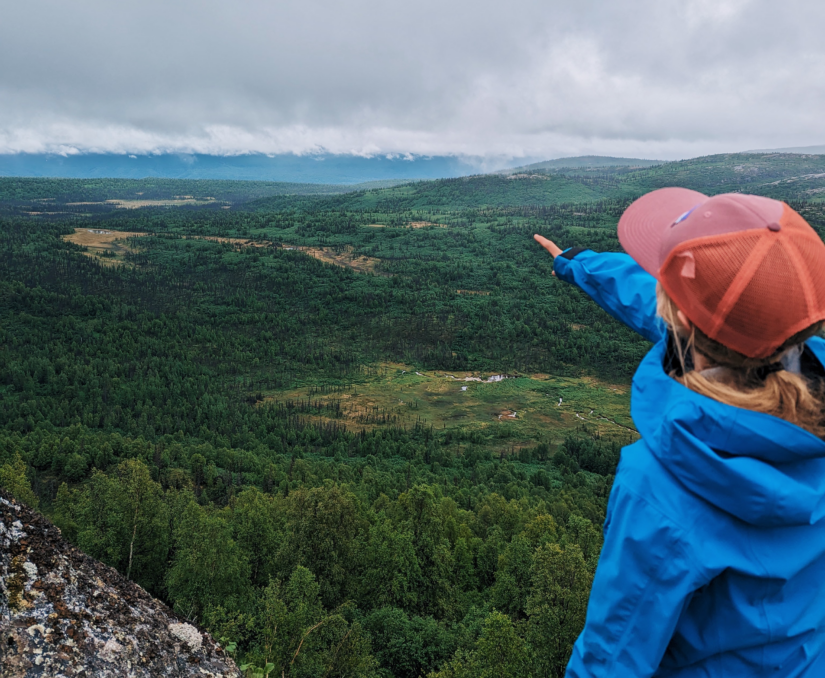 Person in a baseball hat point out to the horizon of a vast valley in Alaska.